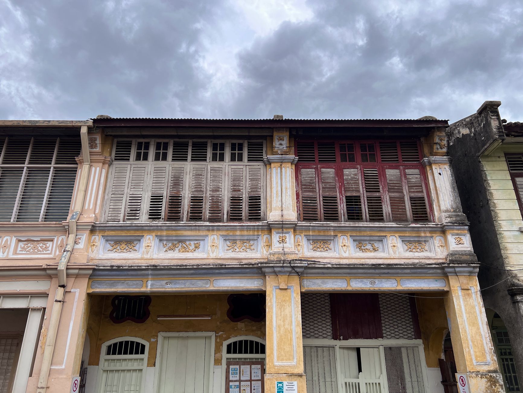 Weathered George Town shophouse row with timber louvre shutters and ornate stucco