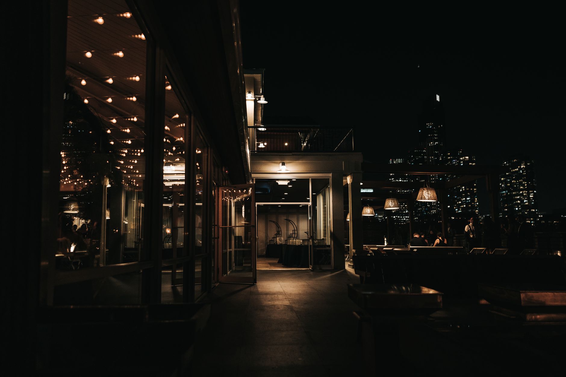 Rooftop terrace at night strung with warm bulb lights above the city