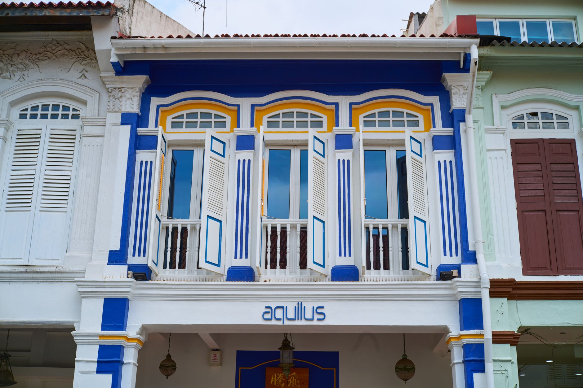 Restored blue-and-white Straits shophouse facade with arched louvre windows